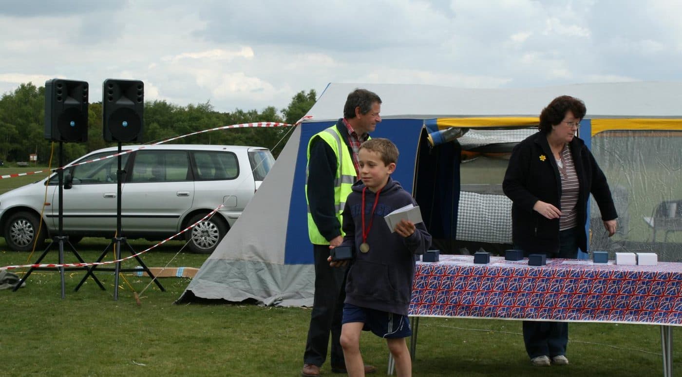 A boy in a hooded top walks away from the prize table at the Silchester fun run, a medal round his neck and a prize in his hand.