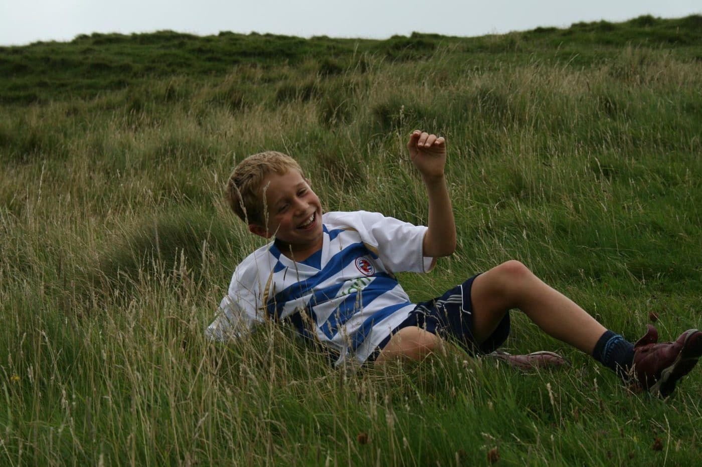 A boy sitting laughing in long grass in a field.