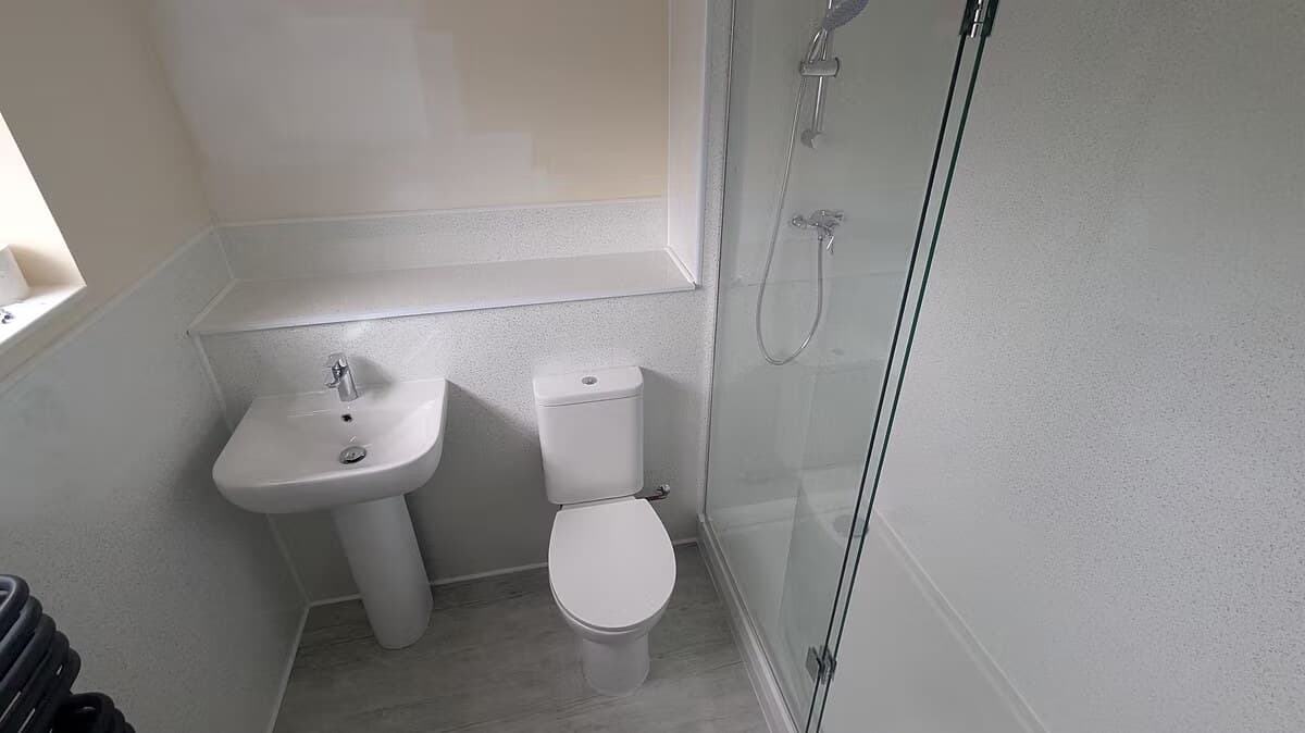 A finished shower room with panelled walls, a pedestal basin and a glass shower screen