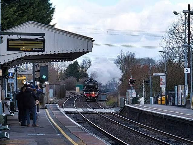 Bramley station with a steam locomotive approaching the platform under the canopy, passengers waiting and the level crossing beyond.