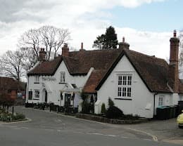 The Crown at Kingsclere, a white painted pub with a dark tiled roof and brick chimneys on a street corner.