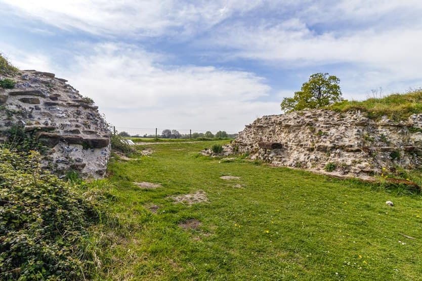A break in the Roman town wall at Silchester, two stretches of flint and tile walling with grass between them and open fields beyond.