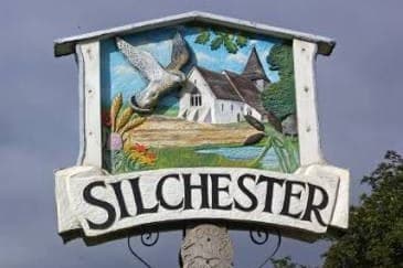 The carved Silchester village sign, a barn owl flying over the church, with the village name on a panel beneath it.